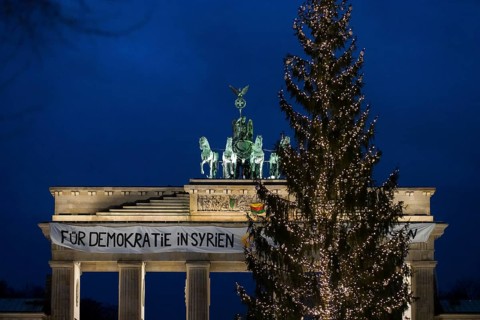 A banner For Democracy in Syria / Defend Rojava hangs behind a Christmas tree at the Brandenburg