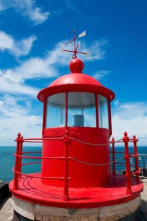 Red lighthouse with round roof on a coastal platform, blue sky and sea in the background, Fort São