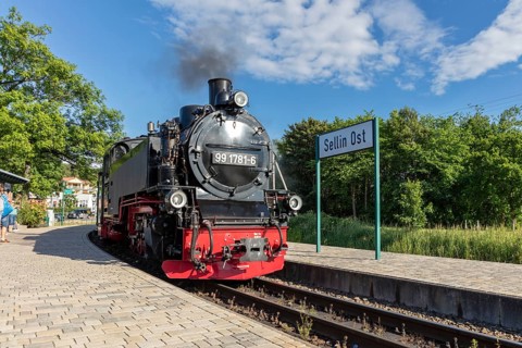 A steam locomotive stands at the railway station with a sign in summer weather, Rügen, Rasender