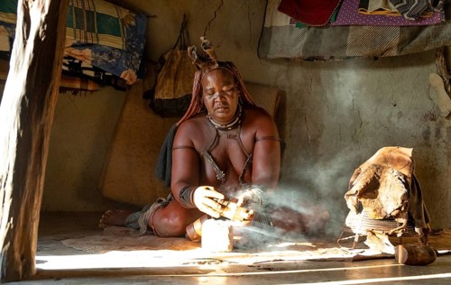 Traditional Himba woman prepares herbs for body care with smoke, Interior of the first woman's mud