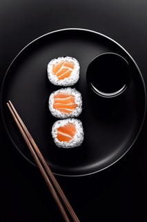Three sushi rolls filled with fresh salmon are neatly arranged on a black plate. A small bowl of