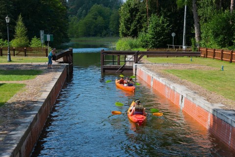Two canoeists on a water canal under a small bridge in a wooded area, Sluza Perkuc, Perkuc lock,