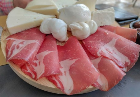 A selection of ham and cheese, arranged on a wooden platter, with buffalo mozzarella in the centre,
