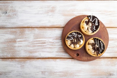 Sweet tartlets with chocolate and cheese cream on a white wooden background. top view, flat lay,