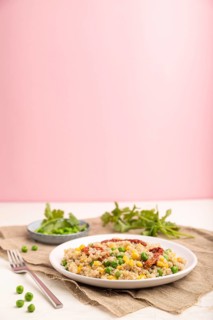 Quinoa porridge with green pea, corn and dried tomatoes on ceramic plate on a white and pastel pink