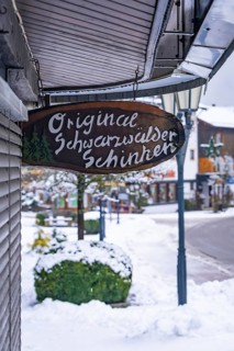Company sign for Black Forest ham on a snowy street with shops, Enzklösterle, district of Calw,
