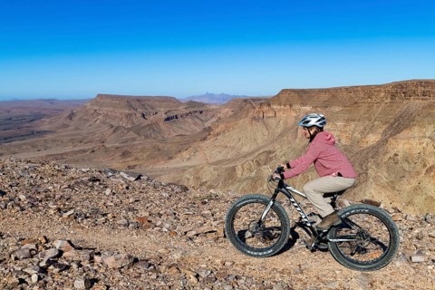 Woman riding a mountain bike, fatbike, on the edge of the abyss, behind the gorge landscape of the