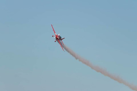 Red stunt aerobatic plane performing stunts in blue sky. Concept of speed, difficulty, precision,