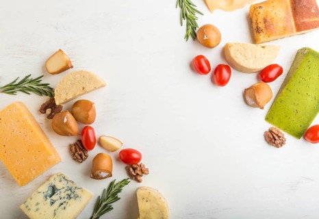 Set of different types of cheese with rosemary and tomatoes on a white wooden background. Top view,