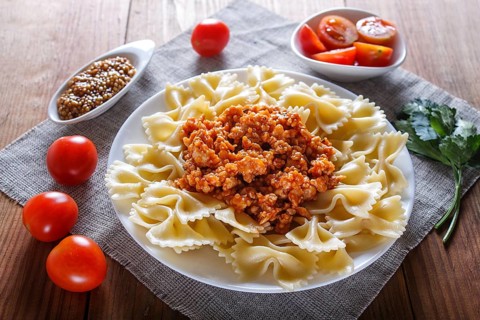 Farfalle bolognese pasta with minced meat on brown wooden background. close up