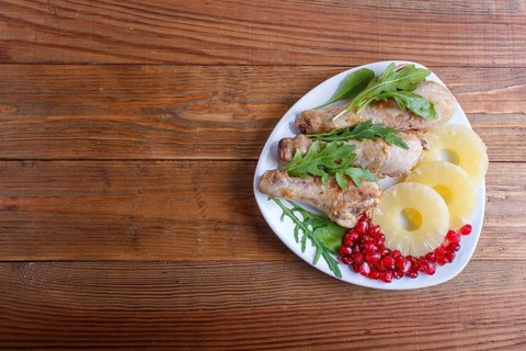 Fried chicken legs with rucola, pineapple and pomegranate seeds on brown wooden background, copy