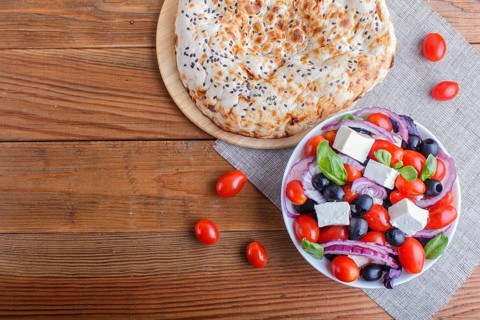 Greek salad with fresh cherry tomatoes, feta cheese, black olives, basil and onion on wooden