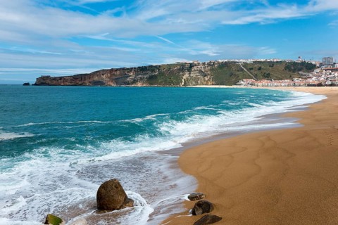 View of the beach coast of Nazaré with waves, sand and a picturesque hill in the background, Praia