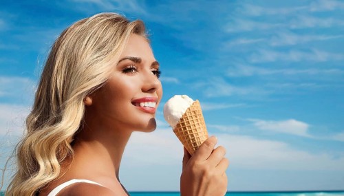 A blonde woman enjoys eating an ice cream in a cone