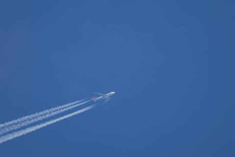 Boeing 747 jumbo jet aircraft flying across a blue sky with a vapour trail or contrail behind,