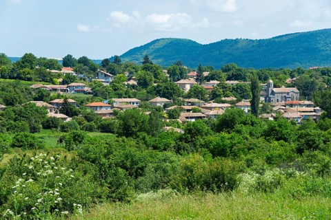 A quiet village surrounded by green hills and trees under a partly cloudy sky, Gagovo, Popovo,