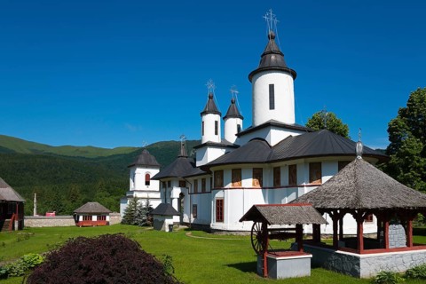 A peaceful Orthodox church with white walls and black roofs in front of a mountain, Cheia Romanian