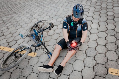Unhappy cyclist sitting on the pavement with knee pain. Concept of a cyclist with knee injury