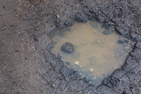 Pothole filled with rainwater on wet black asphalt road surface in spring, Montreal, Quebec,