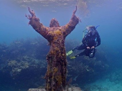 Diver with camera looking at an underwater statue of Jesus Christ (Christ of the Abyss), dive site