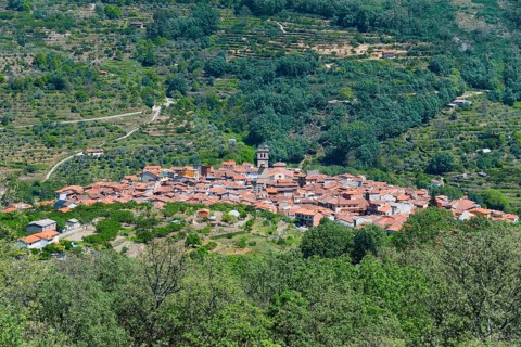 A small village with red roofs in a green valley, surrounded by mountains and dense vegetation