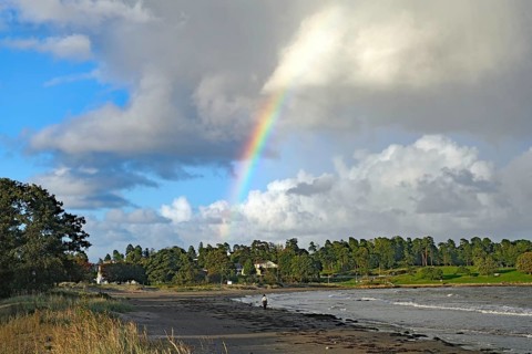 Beach landscape with rainbow and clouds over the sea and green vegetation in the background,