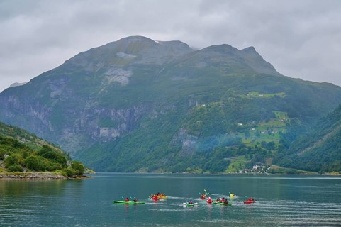 Several kayakers in a fjord surrounded by forested mountains and clouds, Geiranger, Geiranger