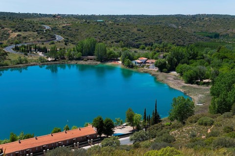 View of a tranquil lake with surrounding houses, trees and hills under a blue sky, view from the