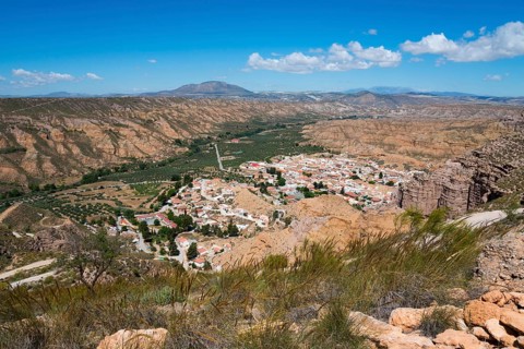 A village with white houses and red roofs, nestled in a dry, mountainous desert landscape under a
