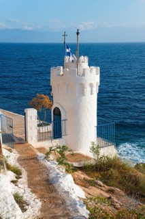 White tower on the coast with a Greek flag surrounded by the blue sea, Church of Agios Nikolaos
