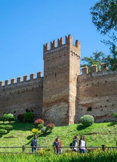 People walk in front of a tower on the defense wall of the medieval Gradara castle, Marche region,