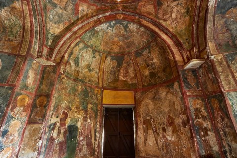A church interior with frescoes on the walls, religious art and a large wooden door, Byzantine