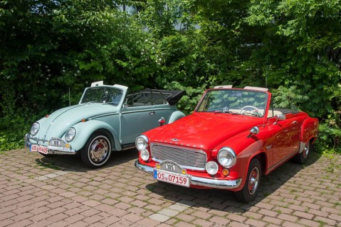 Two classic convertibles, one red and one light blue, parked next to each other on a paved car