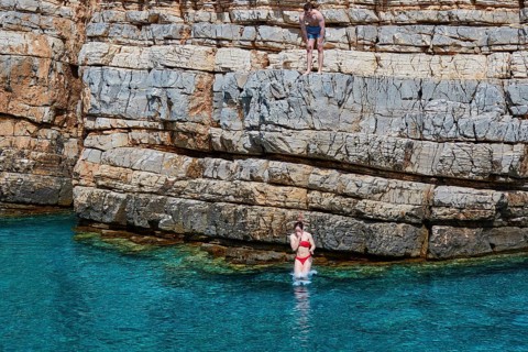 Palatia Beach, Palatia, A person jumps from a rocky cliff into the turquoise water, another person