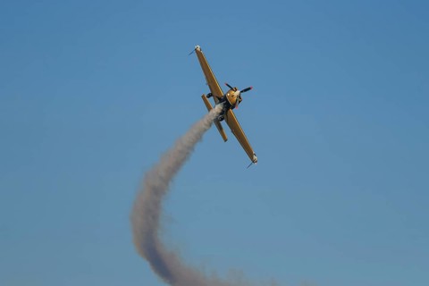 Golden stunt aerobatic plane performing stunts in blue sky with smoke trail. Concept of speed,