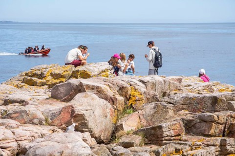 People on rocks by the sea with speedboat in the background in Gudhjem, Bornholm, Baltic Sea,