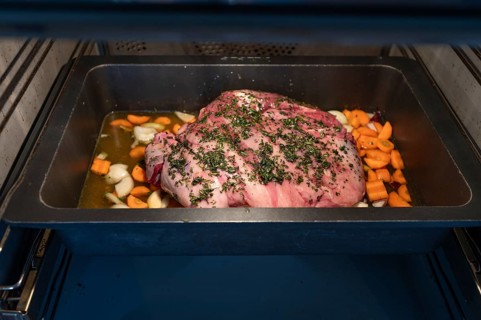 Preparation of a wild boar roast with spices and vegetables in a cast-iron casserole in the oven,
