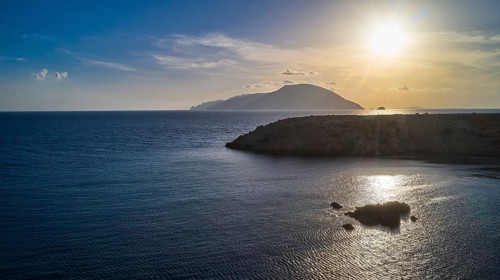 Sunset over the sea with a visible island and calm water, Kassos Island, drone shot, evening light,