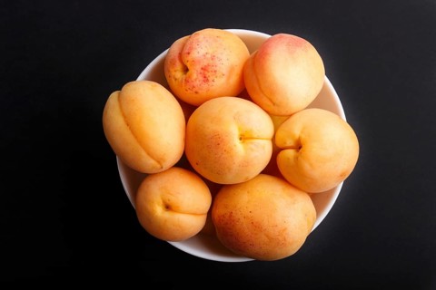 Fresh orange apricots in white bowl on black background. top view, flat lay, close up