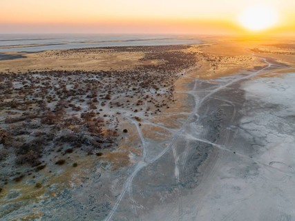 Rocky island with baobab trees in a dry salt pan, at sunset, off-road vehicle on the salt pan,