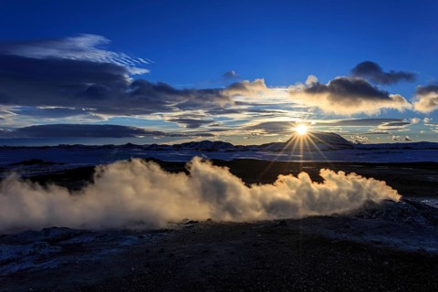 Hot springs and geothermal area in front of mountain landscape in winter, sunbeams, cloudy mood,