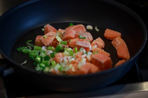 Fry the fresh salmon pieces and chopped spring onions in a black pan on the hob