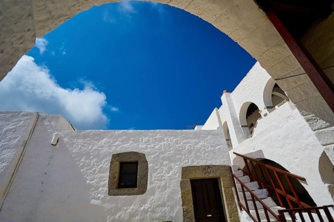 View from below of white buildings and a staircase under an arch in the Greek monastery, Inside the