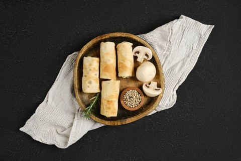 Thin pancakes stuffed with mushrooms on a wooden plate. The rustic setting enhances the appetizing