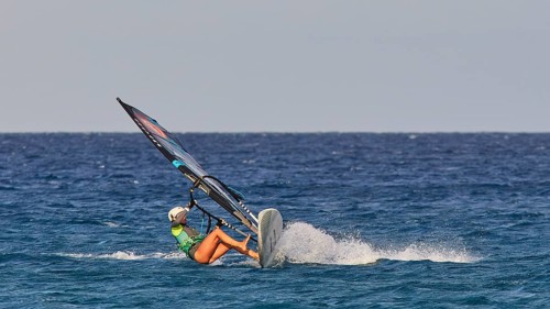 Person in green t-shirt balancing on a wave with a windsurfing board, windsurfer, Meltemi