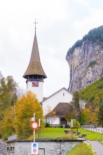 Church with pointed tower in front of rock face and waterfall in an autumn landscape,