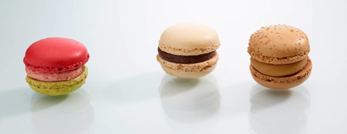 Three differently coloured macarons in front of a white background, studio shot