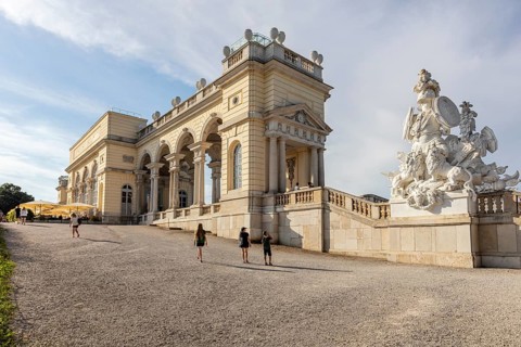 Monumental building with sculptures and columns, in an open area under a blue sky, Vienna