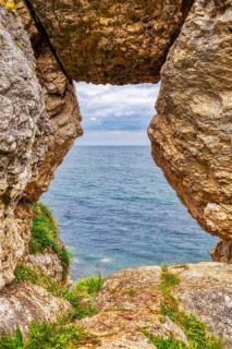 Rock opening overlooking the calm sea under a cloudy sky, Ballycastle