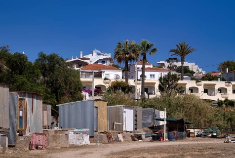 Corrugated iron huts, dwellings of labourers, behind them villas, holiday homes, contrast, poor,